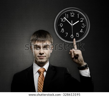 handsome businessman index finger point on clock, on dark grey background