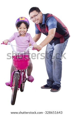 Cute little girl wearing helmet and try to ride a bicycle with her dad, isolated on white background