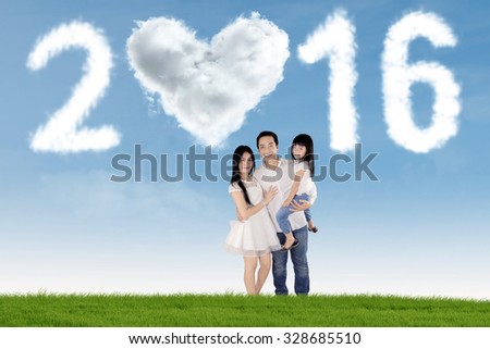 Image of two young parents standing on the meadow with their daughter under cloud shaped numbers 2016