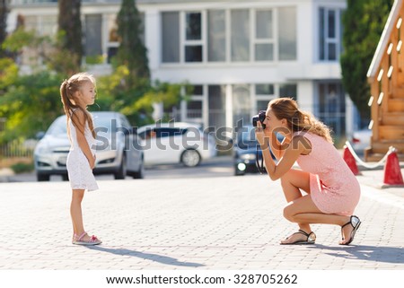 Mother making photos of her daughter child. Mother photograph child outdoor. Mother with camera. Child posing to the camera. Mother photographing her daughter 