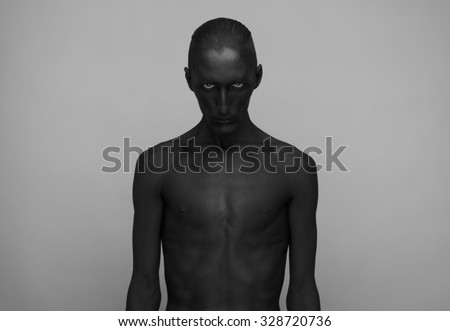 Gothic and Halloween theme: a man with black skin is isolated on a gray background in the studio, the Black Death body art