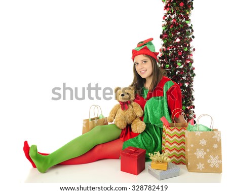 A pretty teen Christmas elf looking at the viewer as she happily relaxes among Santa's gifts.  On a white background with space on the left for your text.