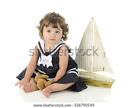 A beautiful barefoot baby looking at the viewer in her sailor dress, a toy sail boat behind her.  On a white background.
