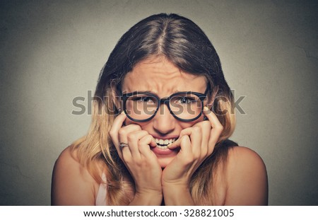 Closeup portrait nervous stressed young woman girl in glasses student biting fingernails looking anxiously craving something isolated on grey wall background. Human emotion face expression feeling Royalty-Free Stock Photo #328821005