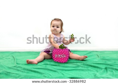 Expenses for raising a child is represented by this baby pulling dollar signs from her bank.  Bank is round, pink with dots.  She is sitting on a green blanket and holding a dollar sign in her hand.