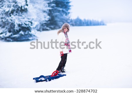 Happy child enjoying a sleigh ride. Child sledding. School kid riding a sledge. Children play outdoors in snow. Kids sled in the Alps mountains in winter. Outdoor fun for family Christmas vacation