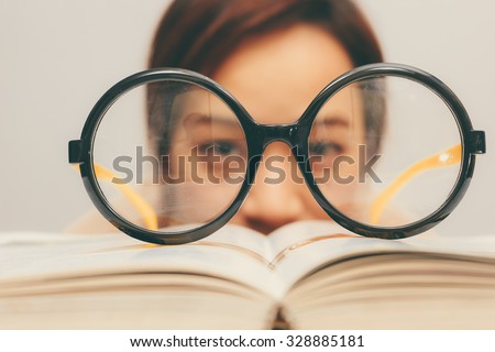Nerdy young asian woman student with old big round glasses bored with reading book + vintage filter