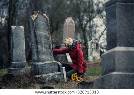 Lonely Sad Young Woman in Mourning with Sunflowers Touching a loved one's Gravestone in a Cemetery Royalty-Free Stock Photo #328915013
