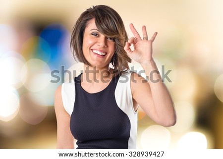 Pretty woman making Ok sign on unfocused background