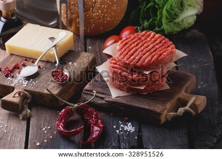 Raw Ground beef meat Burger steak cutlets with seasoning, cheese, tomatoes, salad and bun on vintage wooden boards, black background