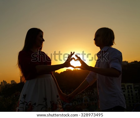 Young couple make the sign of hands hearts in the air before sunrise. Silhouette at sunset. Sweethearts. Love Story. Young couple in love.