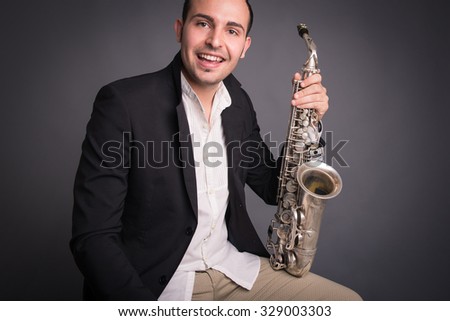 Smiling saxophonist man isolated against dark background. Close up studio portrait.