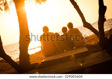 Silhouette of family sitting down on a wooden pallet and watching the sunset. Parents and children relaxing together and enjoying the nature during holiday at the seaside