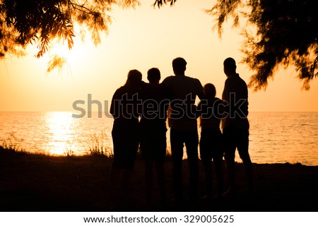 Silhouette of a big family holding each other and watching a beautiful sunset at the seaside in Greece. Concept of traveling together and enjoying the outdoors and the nature