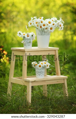 Beautiful camomile flowers in a vaseon green bokeh background. Summer or spring beautiful garden with daisy flowers and garden wooden furniture