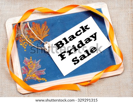 Rough textured blackboard with autumn leaves drawn on one side with a Black Friday, a super sales event day,  message included. The slate blackboard is on a rough textured burlap background
