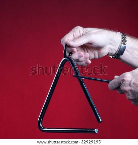 A musical triangle being played by hands isolated against a red background in the square format with copy space.