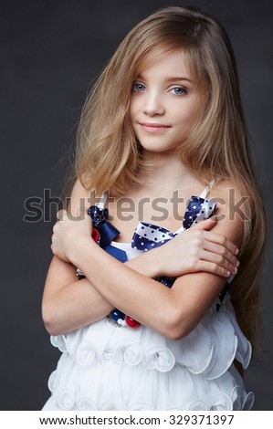 Portrait of happy young girl with crossed hands in white dress over grey background.