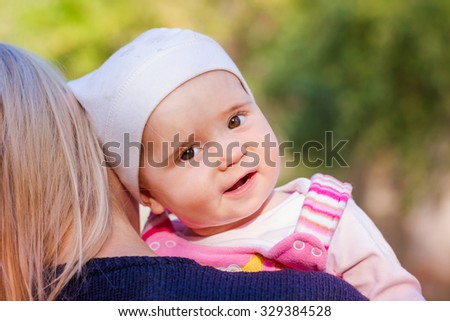 Cute baby girl looking out from mother's back on mother's hands