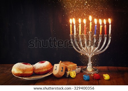 image of jewish holiday Hanukkah with menorah (traditional Candelabra), donuts and wooden dreidels (spinning top). glitter night background
