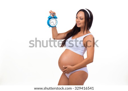 Happy pregnancy. Smiling pregnant woman holding alarm clock. Horizontal photo on white background.