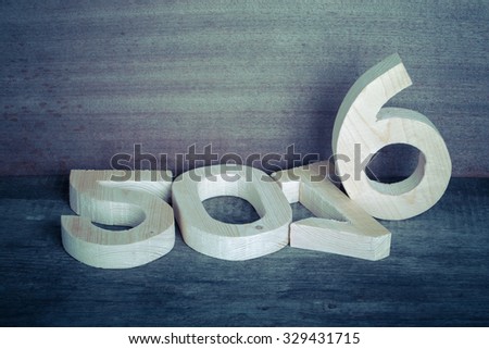 Light wooden figures 2016 on gray wooden background in retro vintage style. Space for text. Toned.