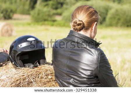 Portrait of woman behind without a face wearing black leather jacket staying near the bale of straw against black helmet.
