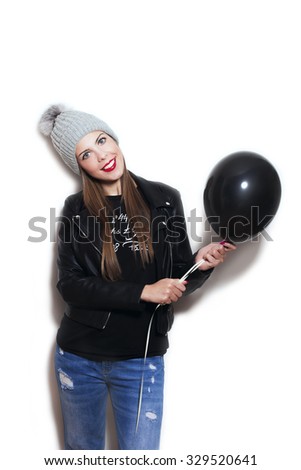 smiling young woman wearing wool cap,  blue jeans and leather jacket  hold black balloon, studio white