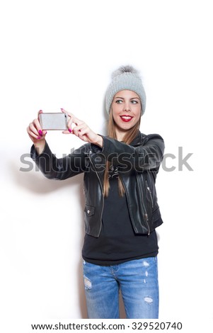 smiling young woman wearing wool cap,  blue jeans and leather jacket  take selfie with smartphone