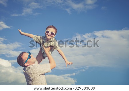 Father and son playing in the park  at the day time. Concept of friendly family. Picture made on the background of blue sky.