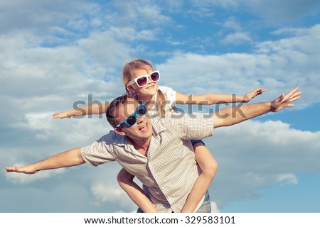 Father and daughter playing in the park  at the day time. Concept of friendly family. Picture made on the background of blue sky.