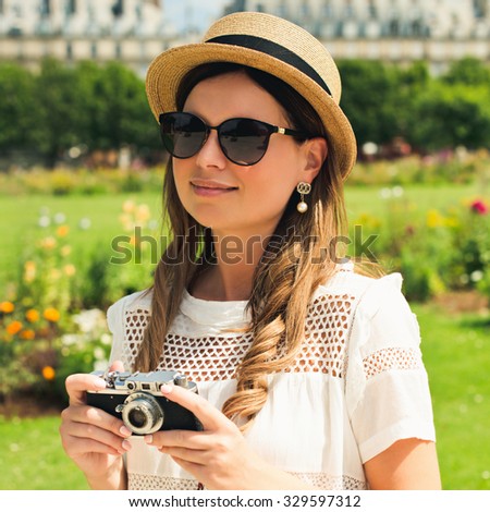 young attractive woman in hat, white dress, red bag and retro camera poses against Paris. Fashion and city style.  