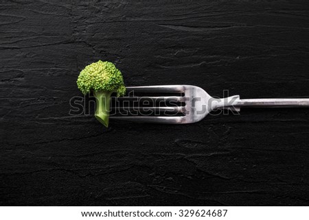 Broccoli with fork on black stone plate background