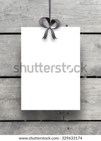 Single hanged paper sheet frame with ribbon on weathered wooden boards background