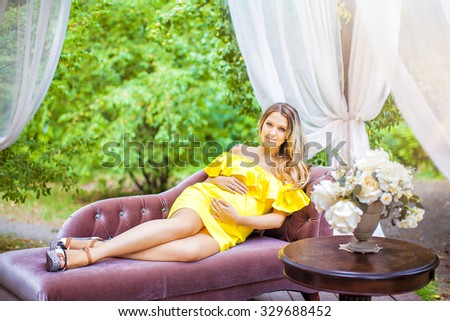 pregnant girl in a yellow dress sitting in the gazebo outdoors