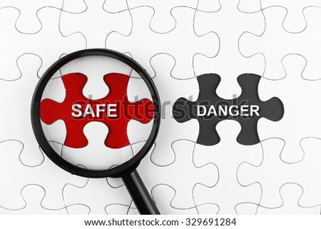 Magnifying glass on missing puzzle with a word Safe and Danger