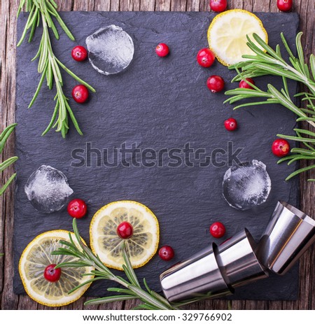 Ingredients for cranberry cocktail with lemon and rosemary on a black stone top view of the board with ice cubes and cocktail metal cups. selective Focus