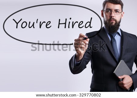 Businessman writing You're hired with marker on transparent board. Business, internet, technology concept.