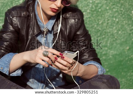 young blond woman with punk style hair using her mobile phone and leaning on green wall 