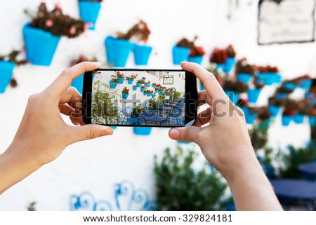 Woman holding a mobile phone to take a picture of picturesque Andalusian facade
