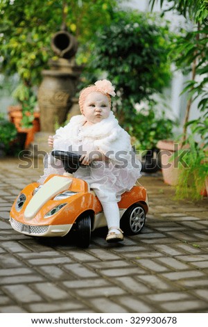 baby girl in a smart dress on a toy car