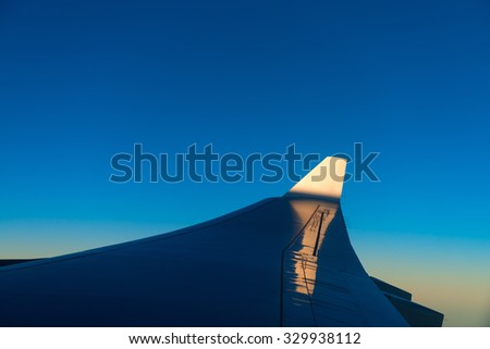 Bold blue sky reflecting of the wing of a commercial airliner as it banks to the left over a cloud bank.