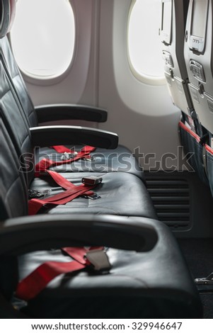 Standard, coach passenger seats on a commercial airliner, with red seatbelt straps crossed and waiting for use.