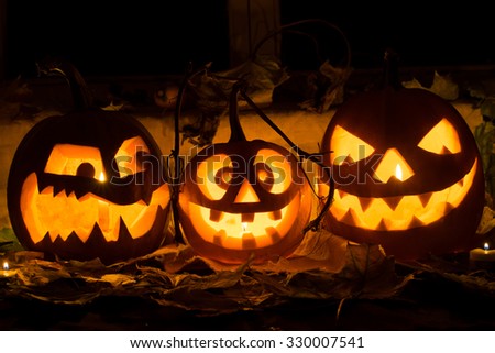 Photo of three pumpkins for Halloween. Embittered, cheerful with a smile and evil pumpkin against autumn leaves and candles