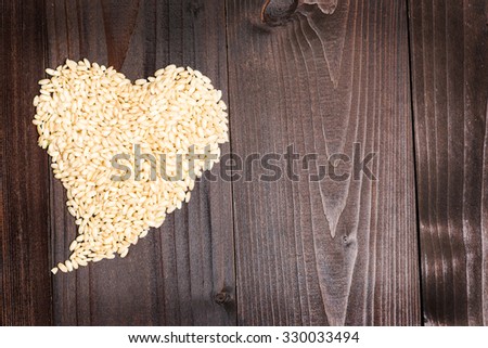 In the picture an heart formed by grains of rice on background of wood with empty space.