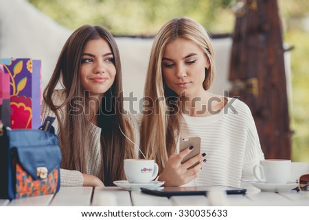 Two young girls using smart phone at the outdoors cafe. 