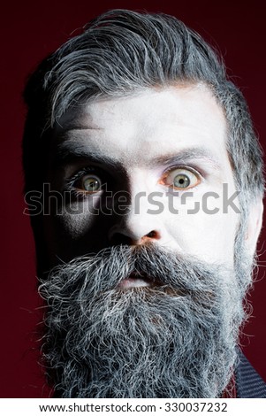 Portrait closeup view of one halloween holiday celebration character emotional man with spooky painted face of zombi and long white lush beard looking forward on purple background, vertical picture