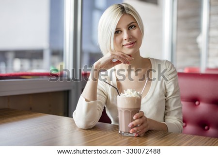 Smiling young woman drinking hot chocolate with cream at cafe