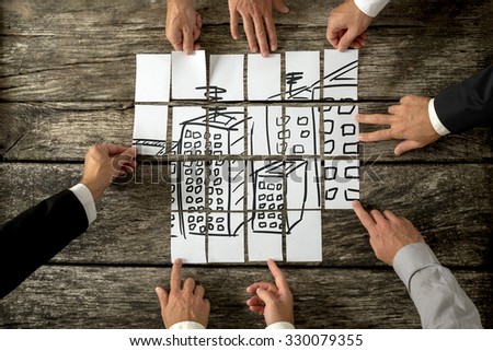 Top view of eight architects or urban planners cooperating in urban development and use of land by assembling hand drawn image of high buildings on white cards. 