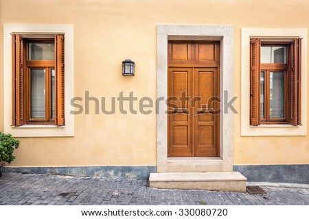 Wood door and windows with wooden shutters on peach colored wall at Santorini, Greece. Royalty-Free Stock Photo #330080720